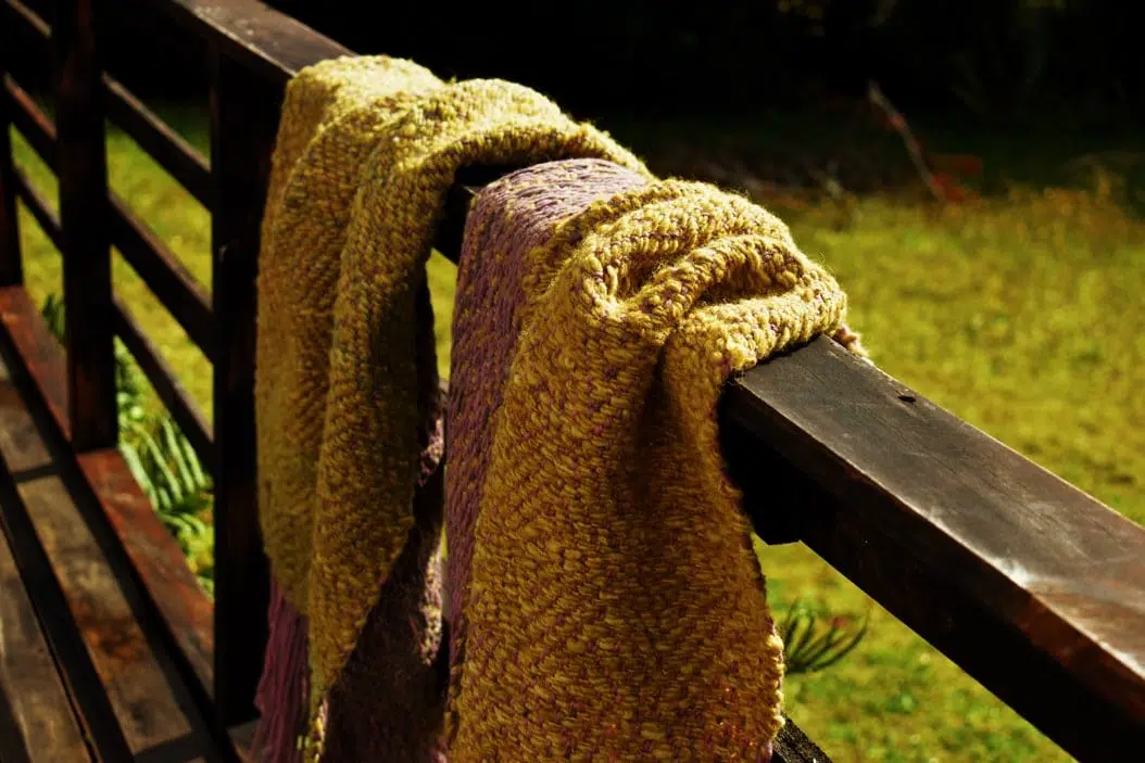 piecera tejida, en color morado y un verde musgo hermoso, esta colgada sobre una baranda, asi puedes ver los dos diseños diferentes que posee este articulo ya que es reversible-