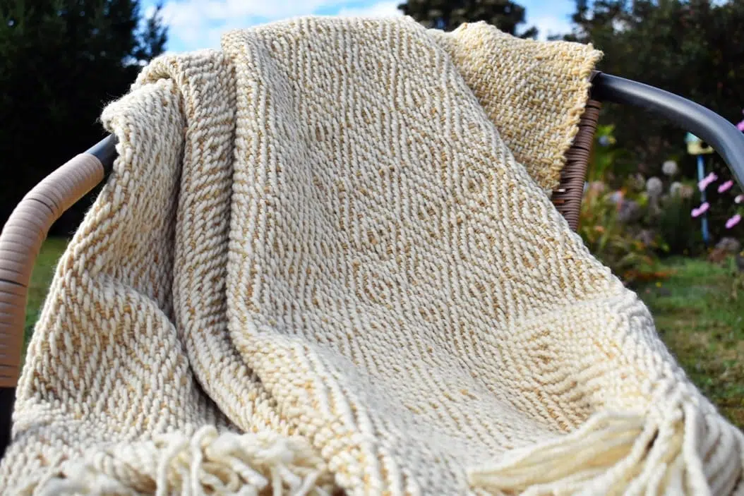 pieceras diseños Piecera tejida a telar piecera en colores muy claros, blanco y beige suave ,esta sobre una silla al aire libre, el diseño es de rombos