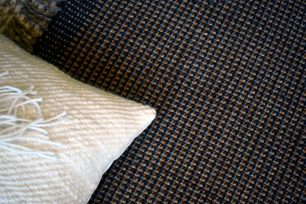 Primer plano de la textura de la alfombra artesanal de lana natural, mostrando el tejido detallado en colores cafés y grises