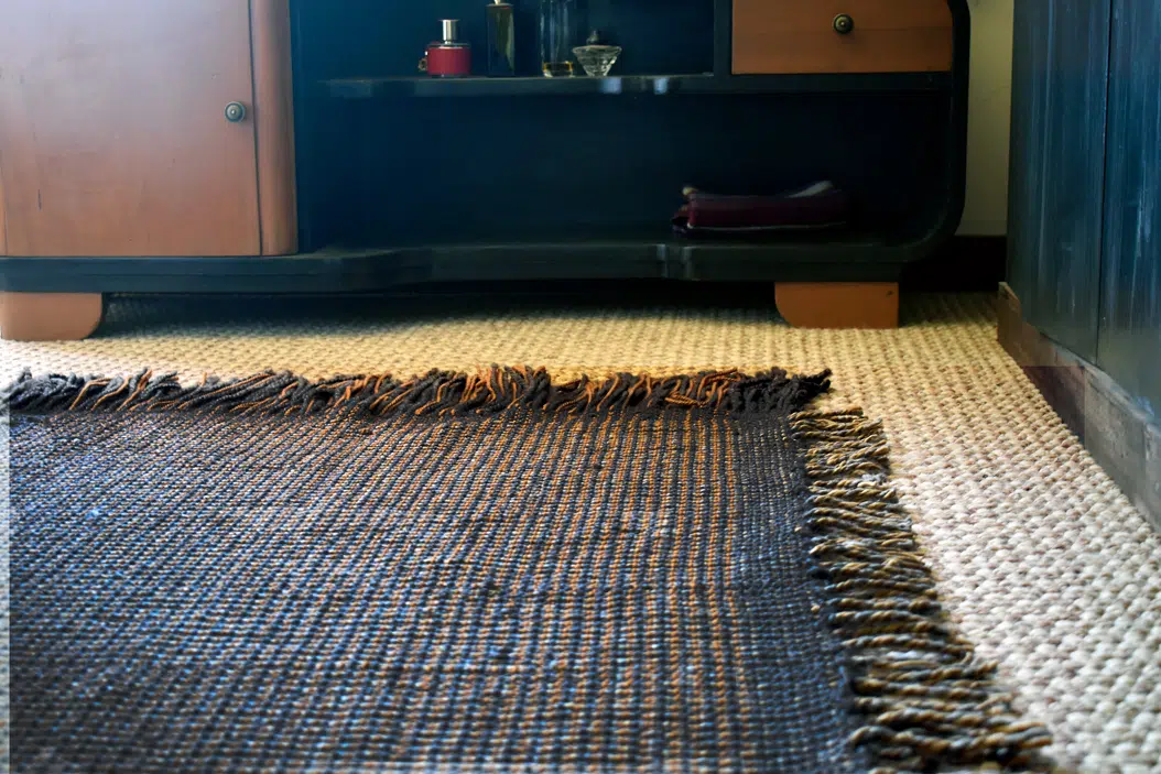 Alfombra artesanal de lana natural en colores cafés y grises, colocada en una habitación con muebles de madera
