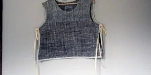 Chaleco de lana natural hecho a mano colgado en una percha, mostrando detalle de los lazos laterales