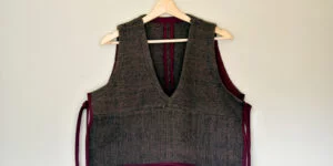 Chaleco artesanal de lana natural colgado en una percha, detalle frontal